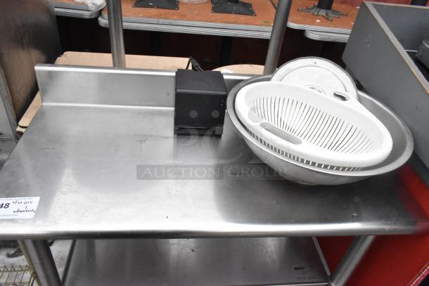 Commercial stainless steel table with backsplash, featuring two under shelves. Includes a colander and small appliance on top.