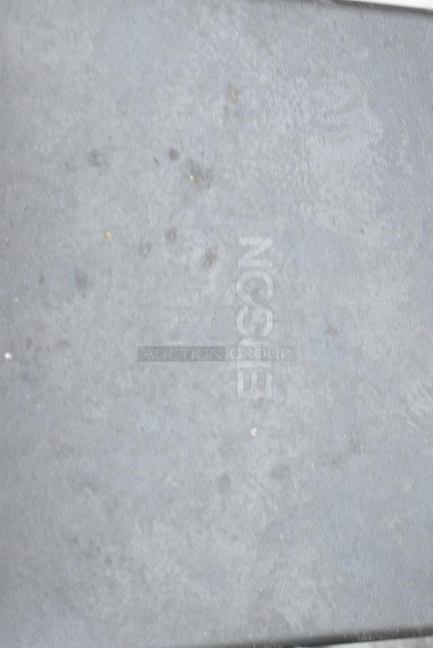 Steel commercial table with backsplash and two under shelves, featuring "Epson" marking. Appears slightly worn.