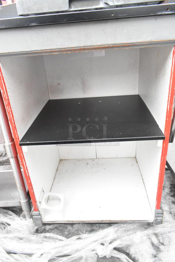 Industrial counter with open shelves, featuring a black surface and red trim, showing signs of wear. Ideal for storage.