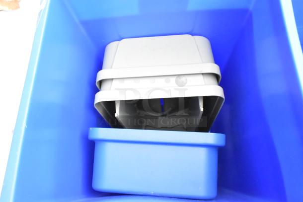 Stacked new slim line trash cans, scratch and dent condition, in blue and gray. Auction includes six units, enhancing value.