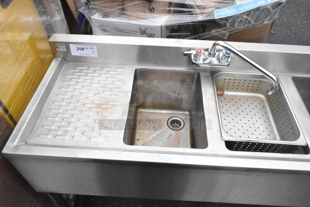 Commercial 4 bay back bar sink with dual drain boards, faucets, handles, and perforated basin insert. Shows wear and markings.