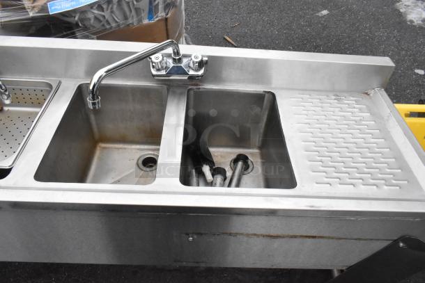 Commercial 4 bay back bar sink with dual drain boards, faucets, handles; stainless steel, used condition, visible cleaning tools.