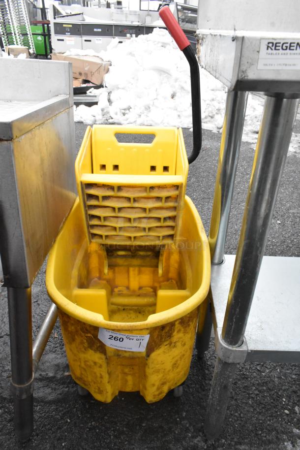 Yellow poly mop bucket with wringing attachment, shows use, visible label with auction info, sturdy handle.