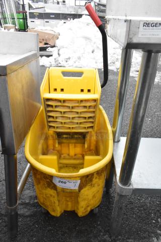 Yellow poly mop bucket with wringing attachment, shows use, visible label with auction info, sturdy handle.