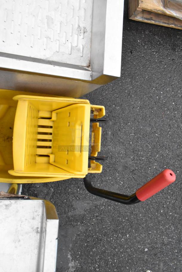 Yellow poly mop bucket with wringing attachment, visible red handle, used condition. Ideal for commercial cleaning.