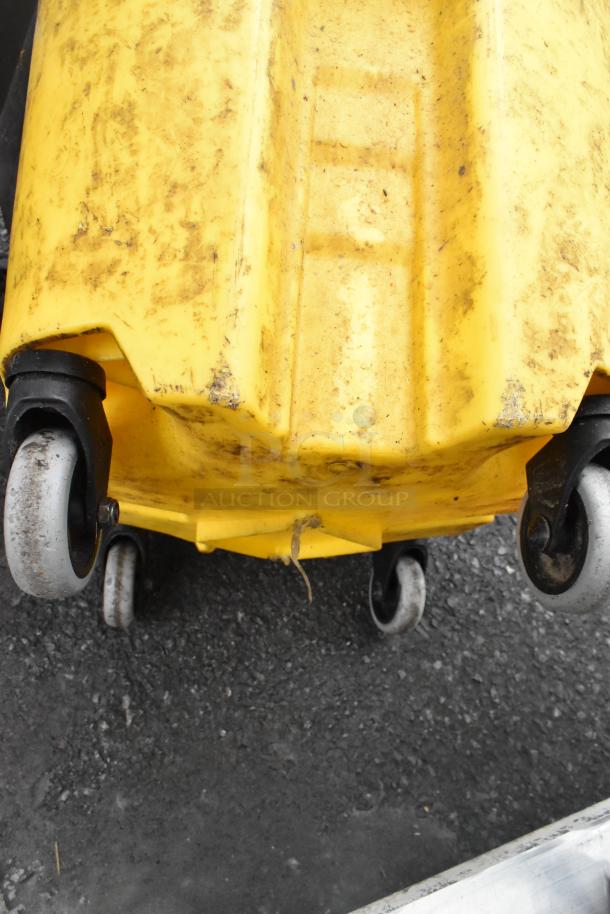 Yellow poly mop bucket with wringing attachment, showing signs of wear. Features durable wheels for easy mobility.