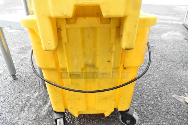 Yellow poly mop bucket with wringing attachment, shows signs of use, features caster wheels for easy mobility.