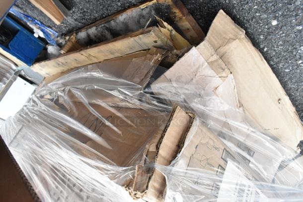 Pallet lot with various items including cardboard boxes, wrapped in plastic. Condition appears mixed, some damage visible.