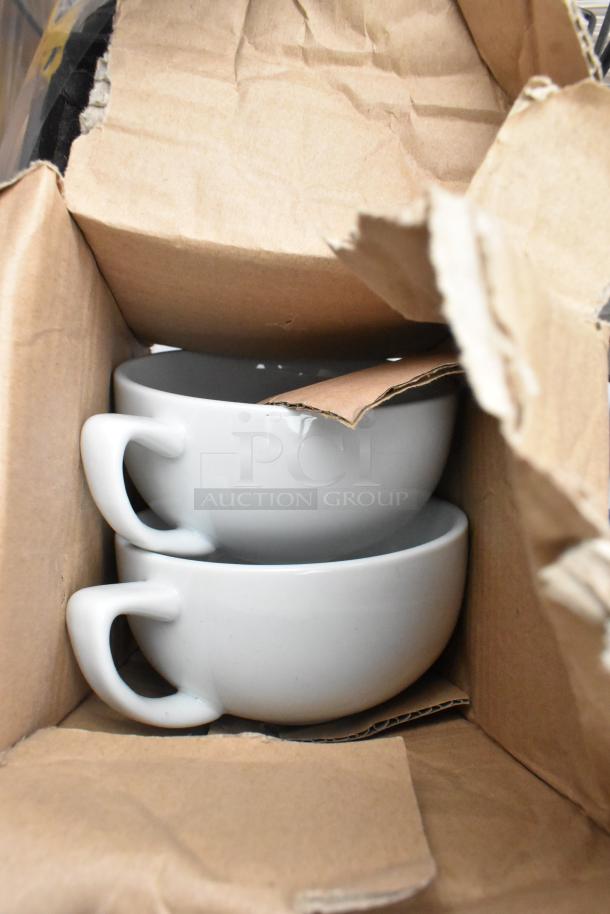 Stacked white ceramic cups in a cardboard box, part of a mixed pallet auction lot.
