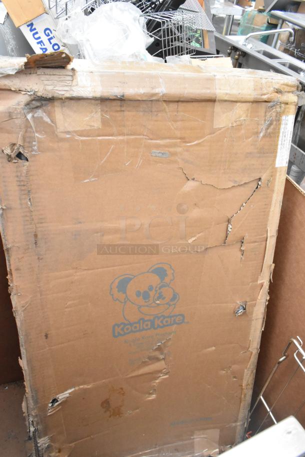 Damaged box with Koala Kare logo containing brand new scratch and dent items, including infant seat kradles and utility sink.
