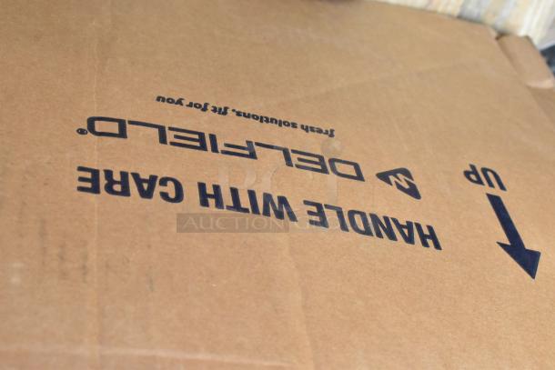 Cardboard box labeled “Handle with Care” containing brand new scratch and dent items, including Avantco over shelf and Watts grease trap.