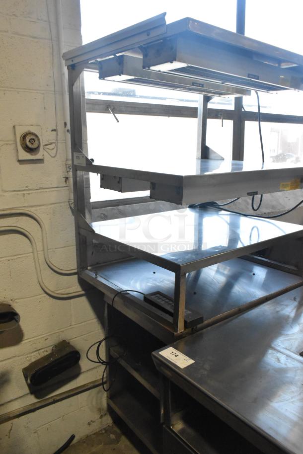 Commercial multi-shelf merchandiser display with warming strips, stainless steel, three-tier, used condition, power cords visible.