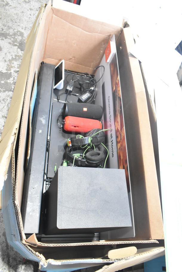 Cardboard box with B Series Soundbar, black and red speakers, tangled cables, and a headset; items appear used.