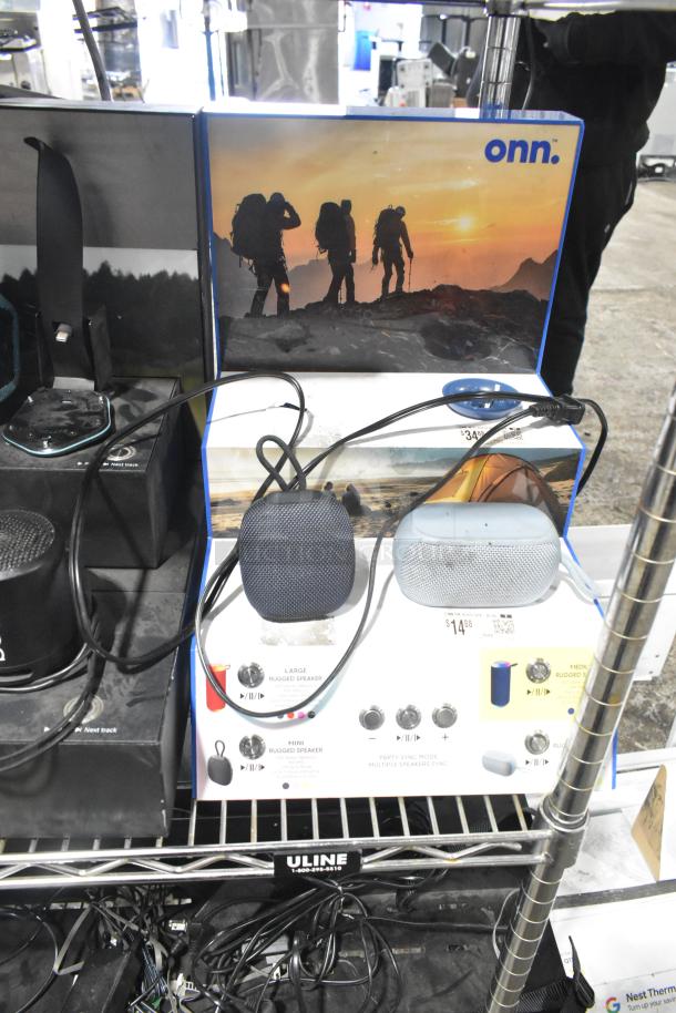 Sony display with built-in speakers and headphones alongside two Onn speakers. Display features outdoor imagery. Items show usage wear.