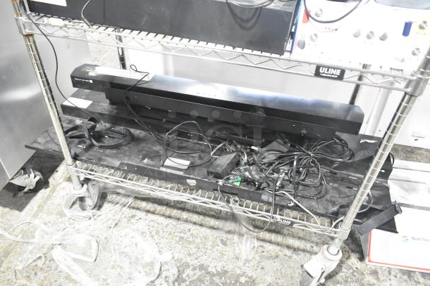 Metal display rack with wheels, multiple shelves, and attached cables. Visible Uline label; used condition.