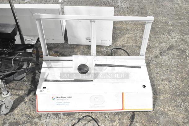 Three white display stands, metal frames, some wear. Sign for Nest Thermostat with bonus trim kit offer visible.