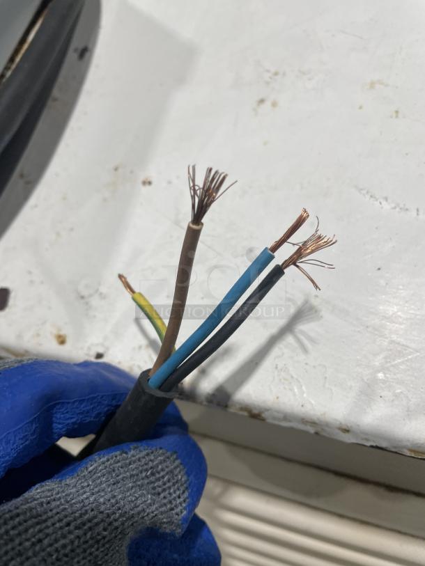 Frayed electrical wires held by a gloved hand. Background shows blurred white and black surfaces.