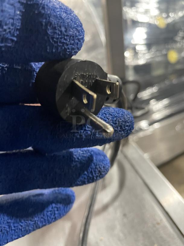 Close-up of a power plug for a Delfield refrigerated prep table, displayed in a gloved hand. Model UCD4464N12DD5.