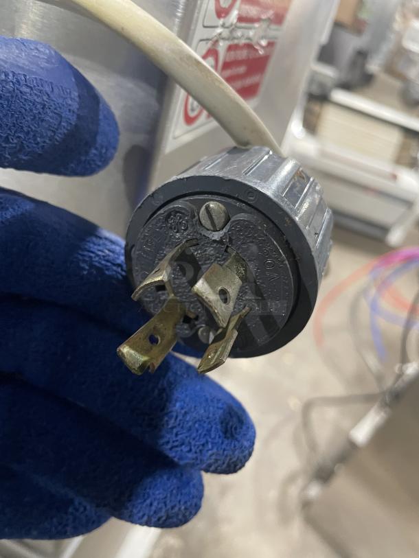 Minipan MGX dough sheeter power plug, 220V 3-phase. Gloved hand holding plug. Part of electric-powered conveyor machine.