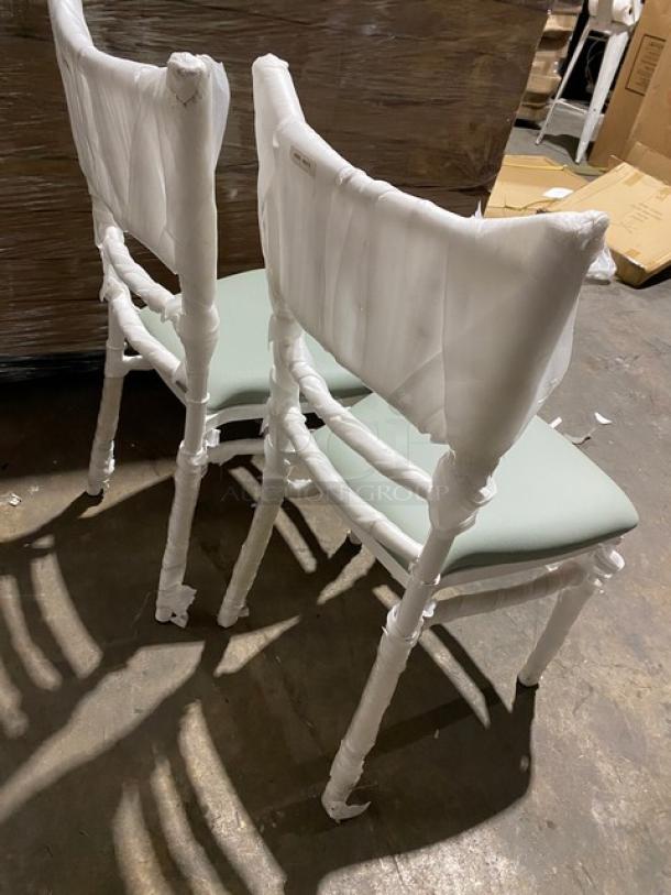 Brand new commercial white resin Chiavari dining chairs with sage green cushions, wrapped for protection.
