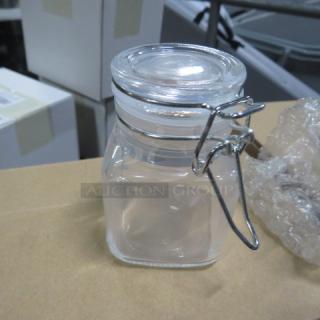 New mini glass spice jar with hinged lid, model 6XBID, in mint condition. Clear glass with metal clasp for secure closure.