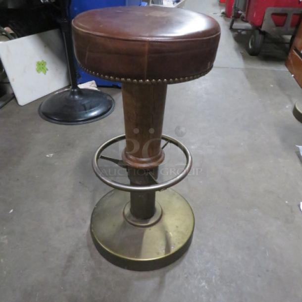 Metal/wood barstool with brown leather cushioned seat, nail head trim, and footrest; sturdy base in good condition.