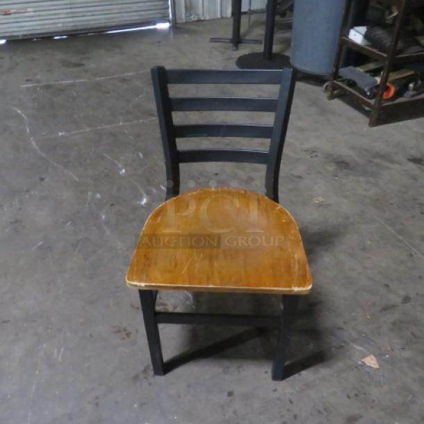 Black metal chair with wooden seat, featuring a ladder back design. Shows minor wear, suitable for dining or decor.