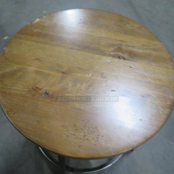 Wooden top of black metal adjustable bar stool with a round design and visible scratches.