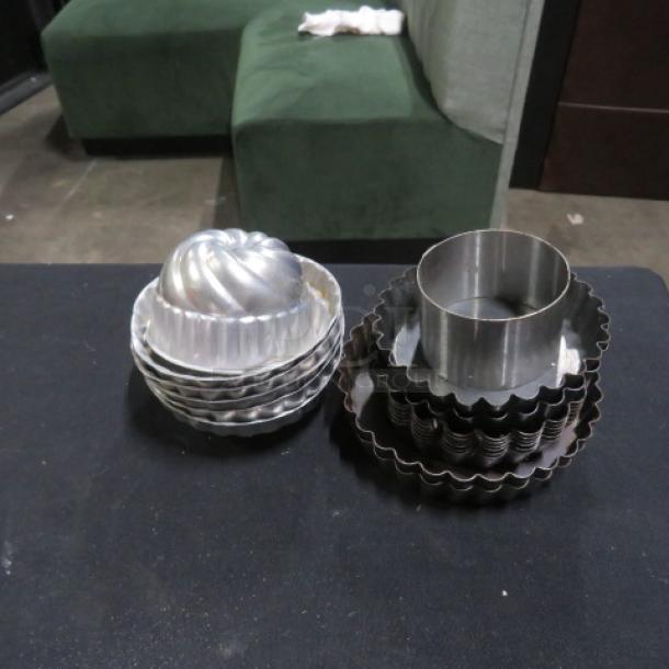 Assorted mini tin molds in varying shapes and sizes, stacked on a table. Good condition, ideal for baking or collecting.