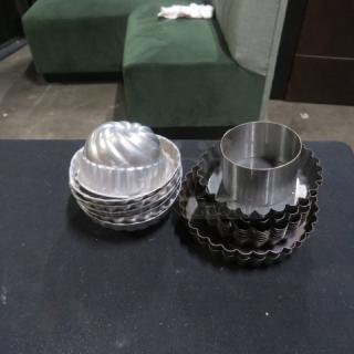 Assorted mini tin molds in varying shapes and sizes, stacked on a table. Good condition, ideal for baking or collecting.