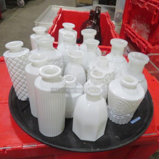 One lot of assorted milk glass tabletop vases/bottles in various sizes and patterns on a black tray. Red bins in background.