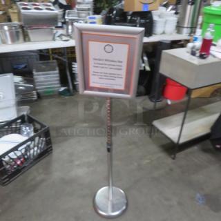 Adjustable sign with silver frame on a pedestal base, holding a printed menu. Used, in good condition. Suitable for displays.