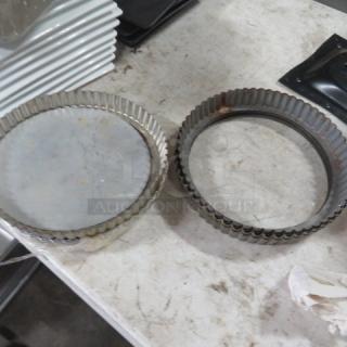 Two metal fluted tart pans, one with a removable base, showing signs of wear, placed on a worn tabletop.