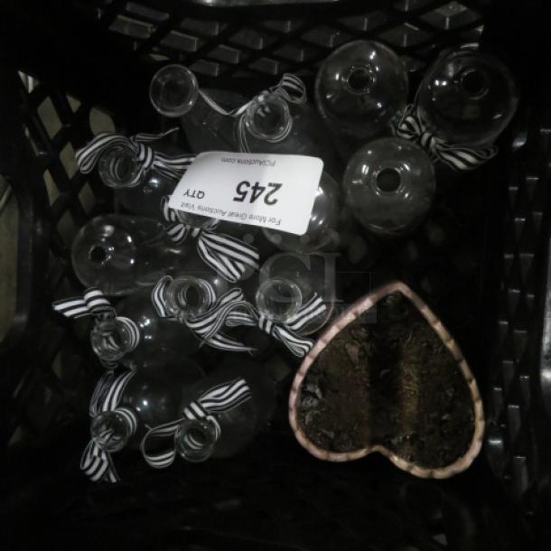 Assorted glass bottles with striped ribbons in a crate, includes a heart-shaped planter with soil. Label reads "245."