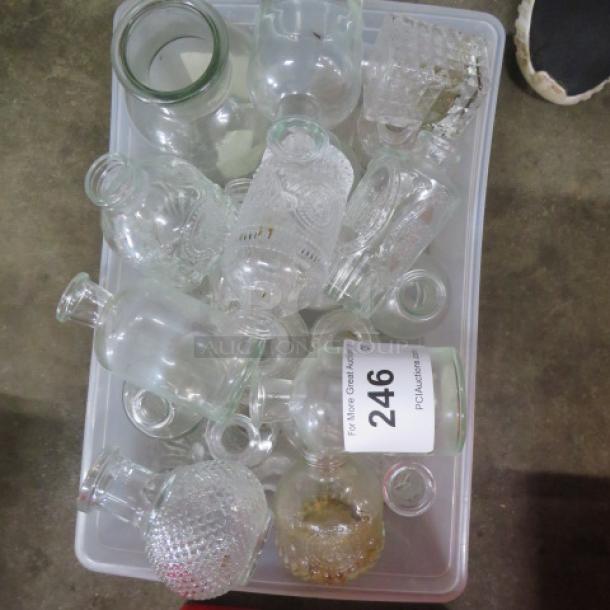 Assorted glass bottles in a bin, varying shapes and sizes, clear and textured designs, with auction label "246".