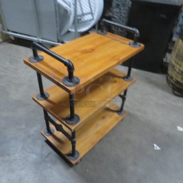 Industrial-style wooden cart with three shelves on casters, measuring 27.5x16x35 inches. Black metal piping detail.