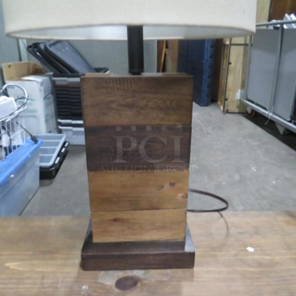 Wooden table lamp with square shade, featuring a block-style base in mixed wood tones. Good condition, minimalist design.