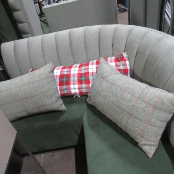 Three assorted pillows displayed on a gray curved sofa; two with a plaid pattern and one with a red and white checkered design.