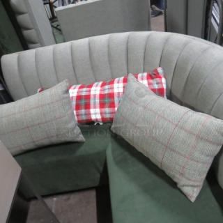 Three assorted pillows displayed on a gray curved sofa; two with a plaid pattern and one with a red and white checkered design.