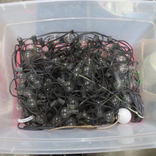 A large container filled with black-corded patio string lights, featuring clear bulbs, in used condition.