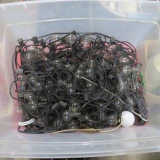 A large container filled with black-corded patio string lights, featuring clear bulbs, in used condition.