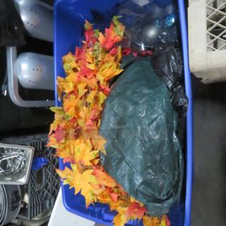 Blue storage bin containing autumn leaves decor and other mixed items. Appears in used condition, ideal for seasonal decoration.