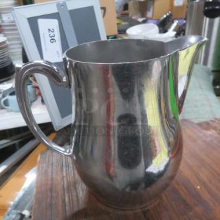 Stainless steel pitcher with handle and spout, reflective finish, in good condition, auction tag number 236 visible.