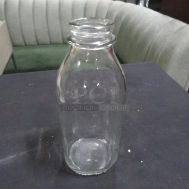 Clear glass milk bottle, 12XBID model, vintage style, in good condition on a dark surface.