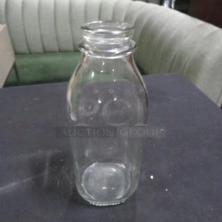 Clear glass milk bottle, 12XBID model, vintage style, in good condition on a dark surface.