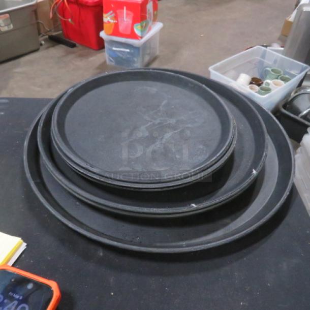 Assorted size black waitress trays, stacked; used condition with surface wear. Model 6XBID.
