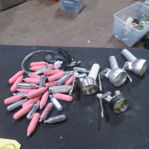 Lot of Whip-Its, including dispensers, pink covers, and cartridges. Assorted items on a black surface, used condition.