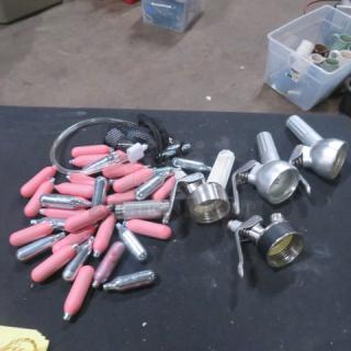 Lot of Whip-Its, including dispensers, pink covers, and cartridges. Assorted items on a black surface, used condition.