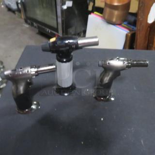 Three assorted hand torches, metal and black plastic, in good condition on display table. Model: 3XBID.