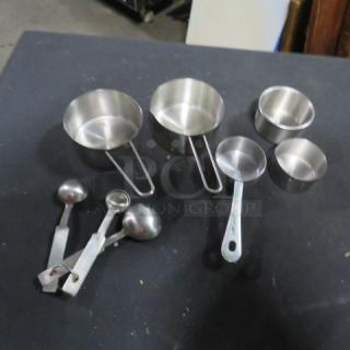 Assorted lot of stainless steel measuring cups and spoons, various sizes, in good condition on dark background.